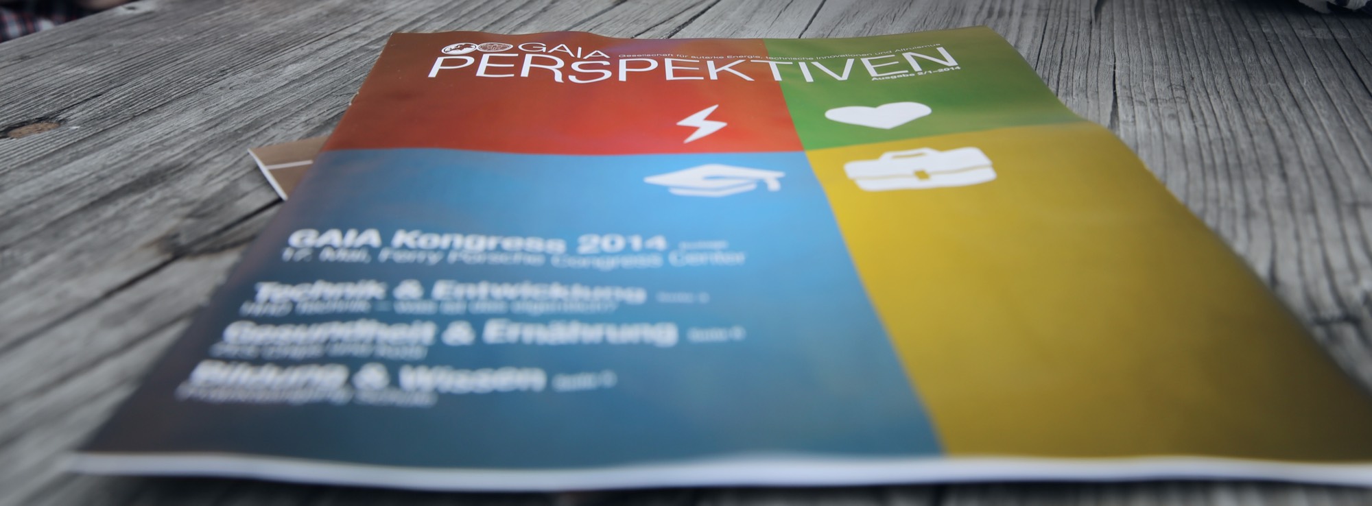 Das GAIA-Magazin „Perspektiven“ mit den vier Themensäulen — Energie, Gesundheit, Bildung und Ökonomie — auf einem Holztisch.